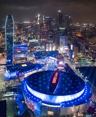 A nighttime aerial view of L.A. LIVE light up bright with the Los Angeles skyline in the background.